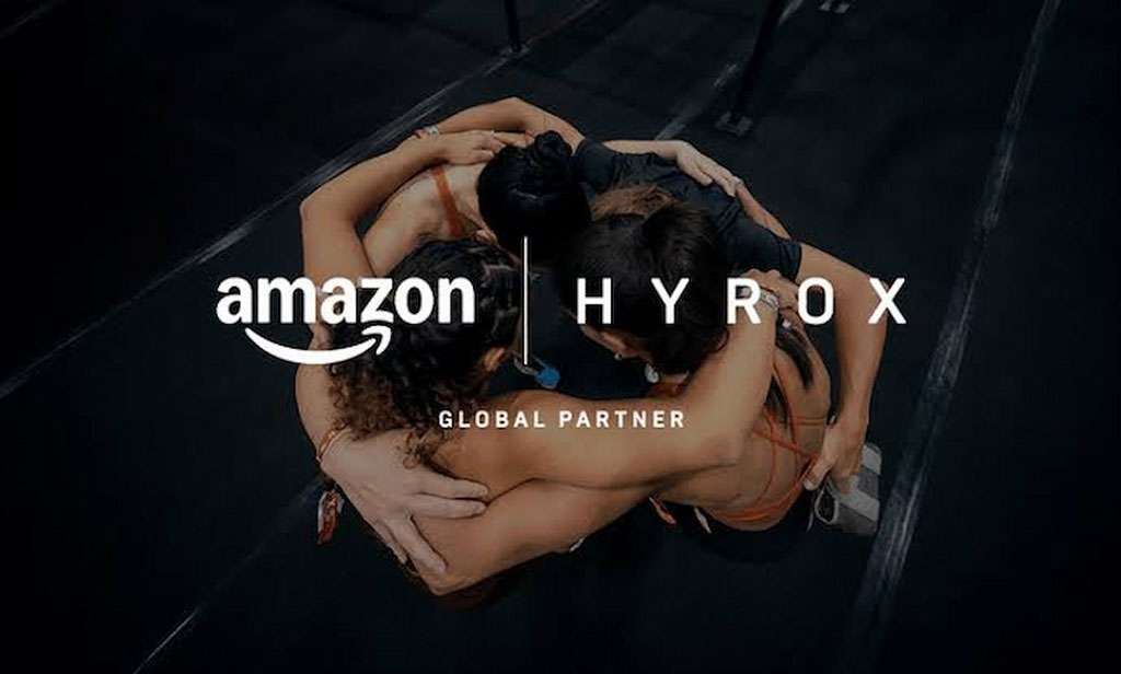 Vista aérea de atletas de HYROX abrazándose con logo de Amazon y HYROX sobre ellos