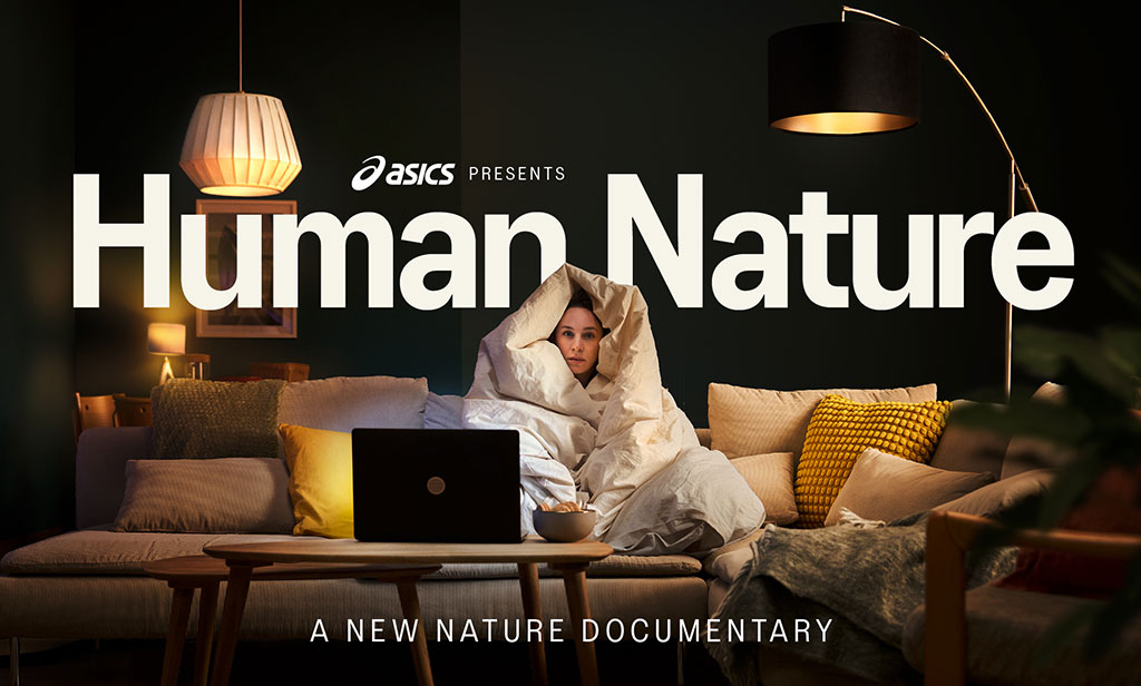 Portada de ASICS Human Nature que muestra una mujer sentada en un sofá tapada con un cobertor y viendo TV en un laptop